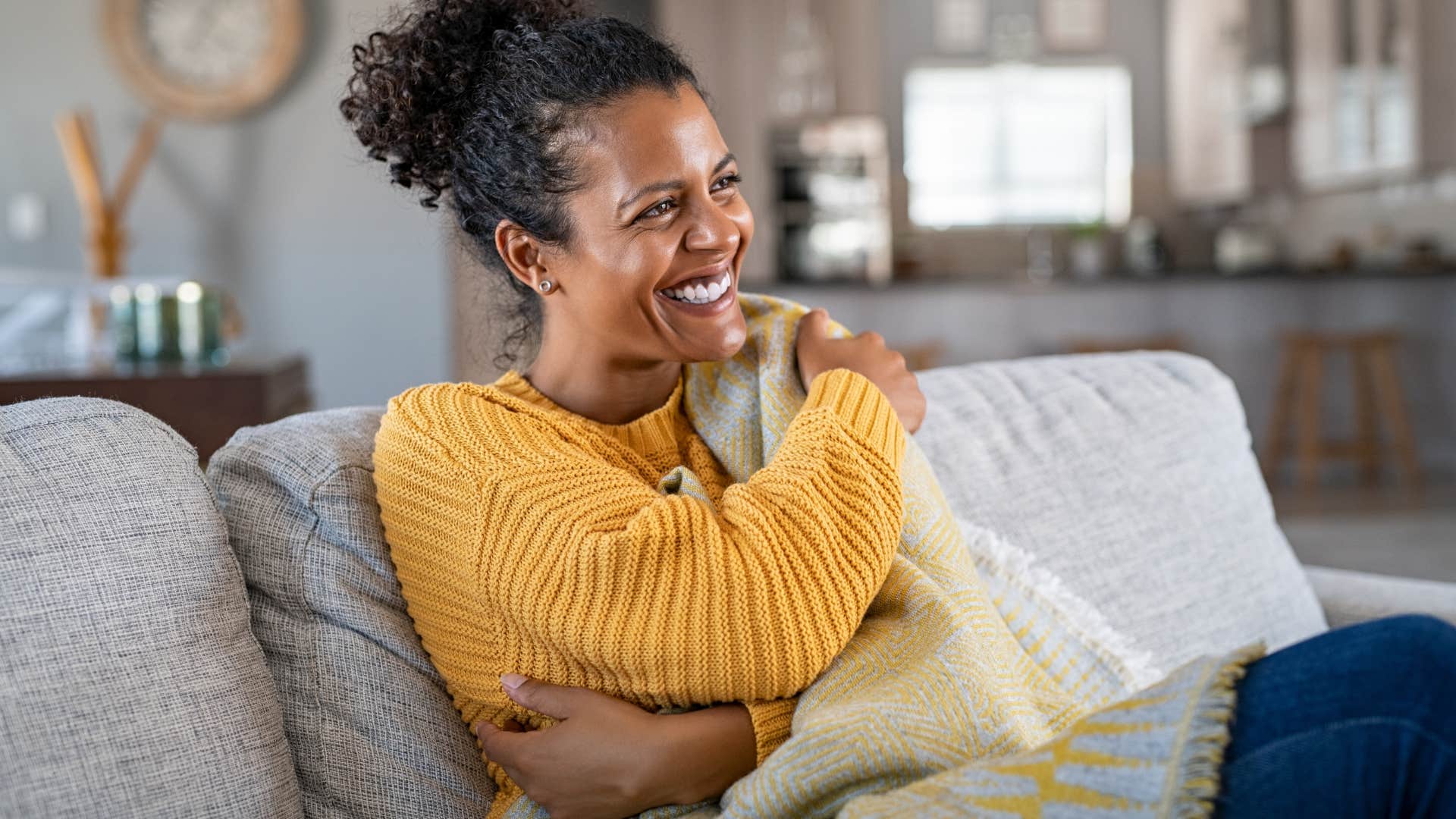 woman relaxing under cozy blankets and pillows on her couch