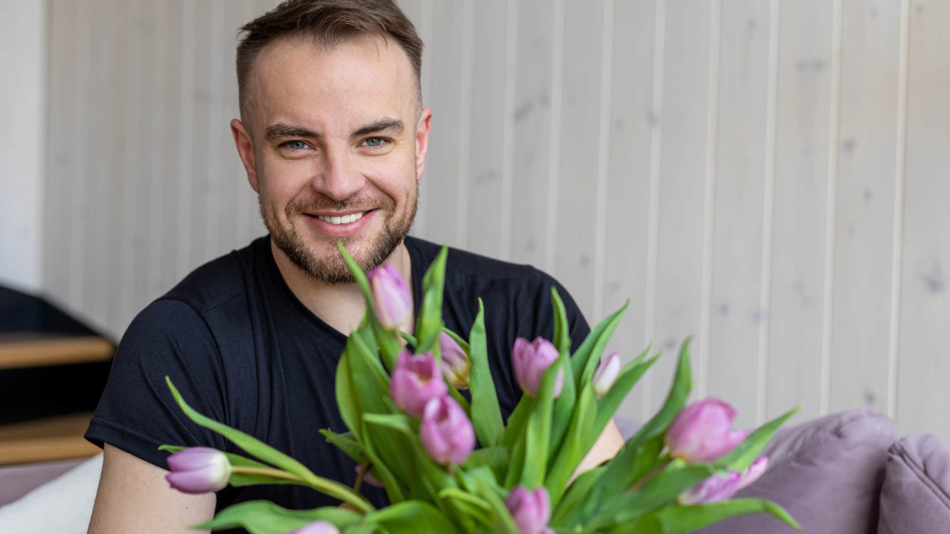 man smiling and smelling fresh flowers at home