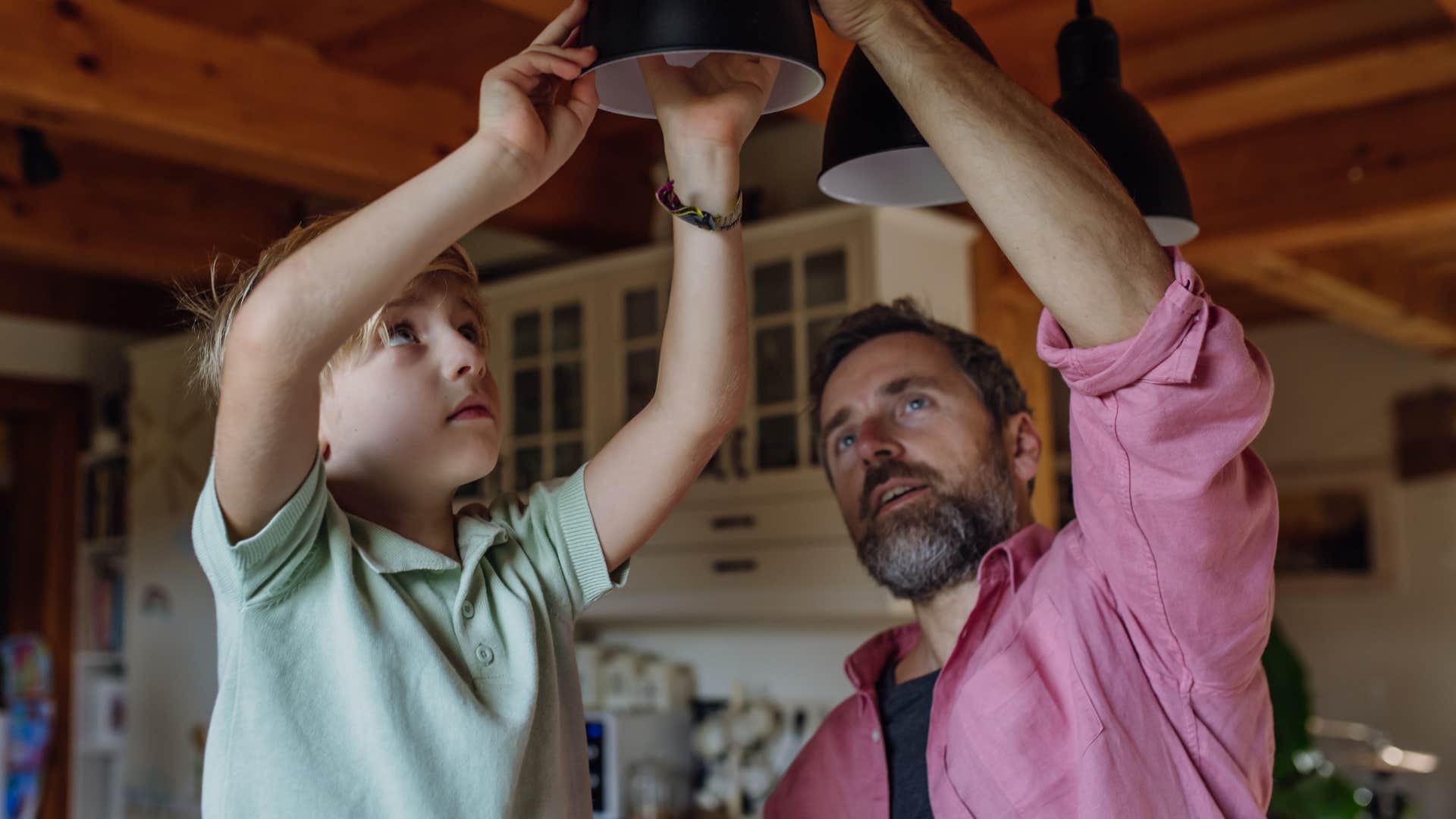 man screwing in an LED light bulb with his young son