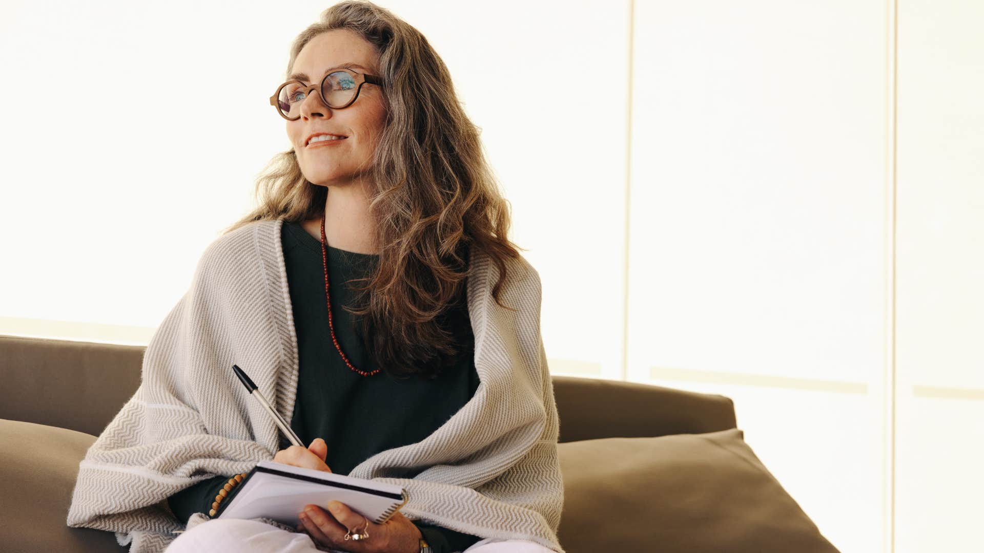 Woman smiling and writing in a gratitude journal at home.