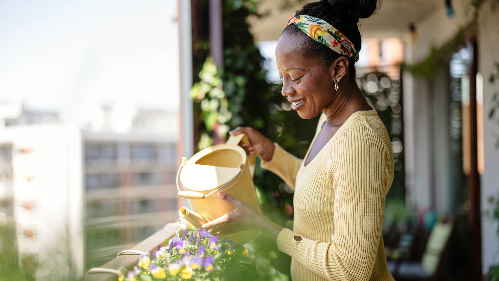 Woman smiling and watering plants on her balcony.