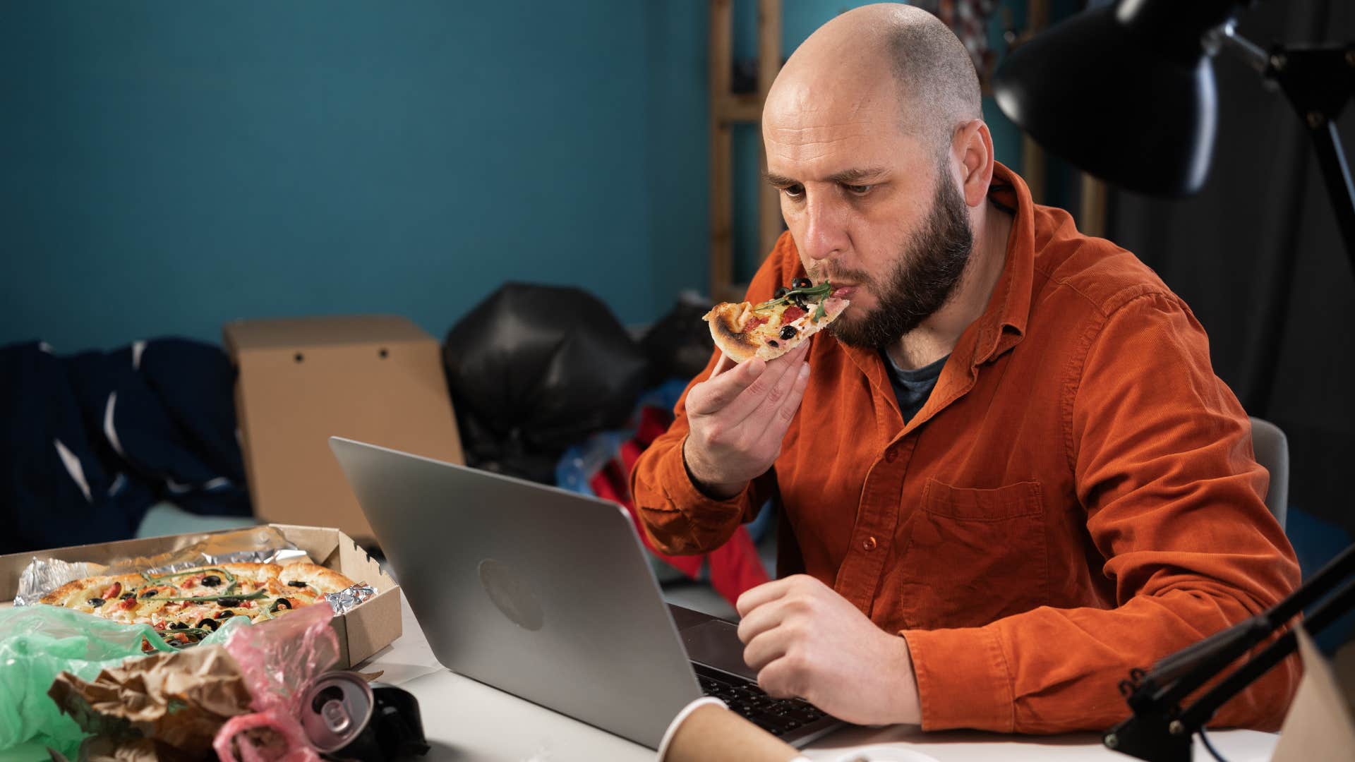 man eating pizza surrounded by unnecessary clutter