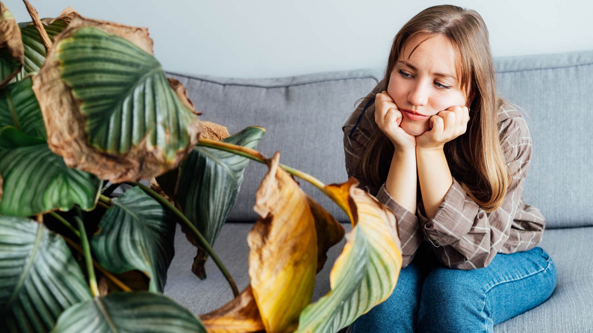 sad woman looking at dead plants in her living room