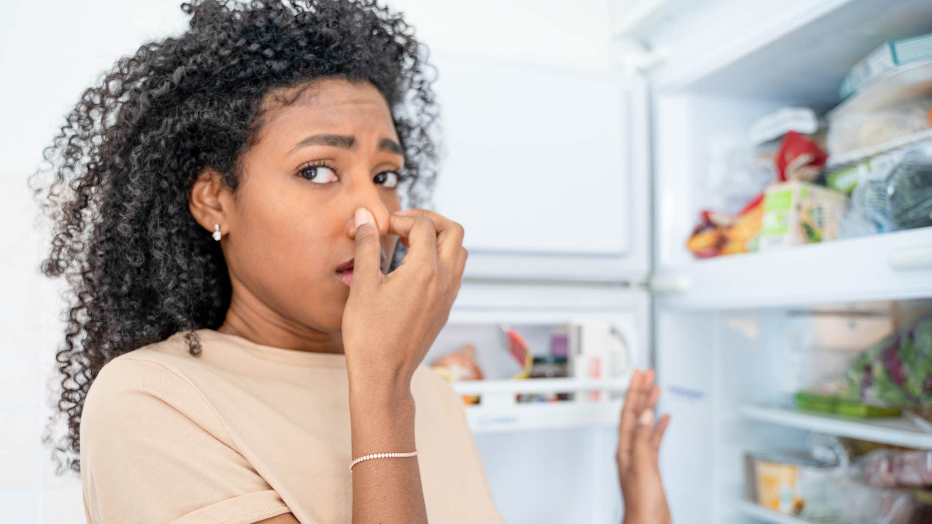 woman holding her nose at outdated or spoiled food in her fridge