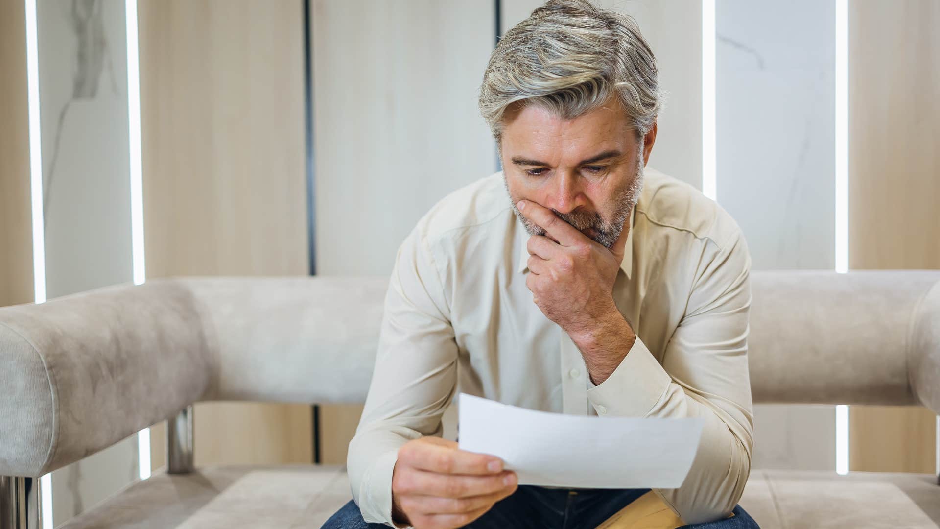 man looking at unopened mail on his couch