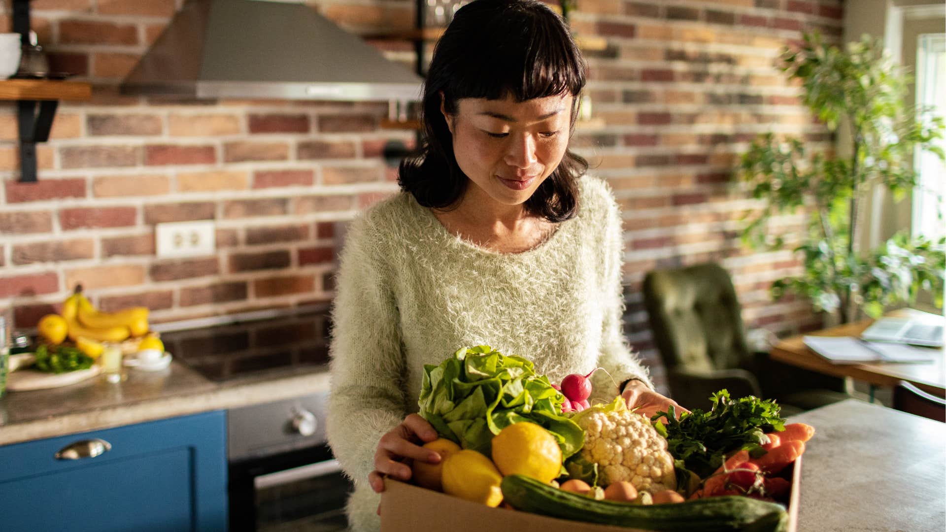 woman smiling at a box of fancy groceries