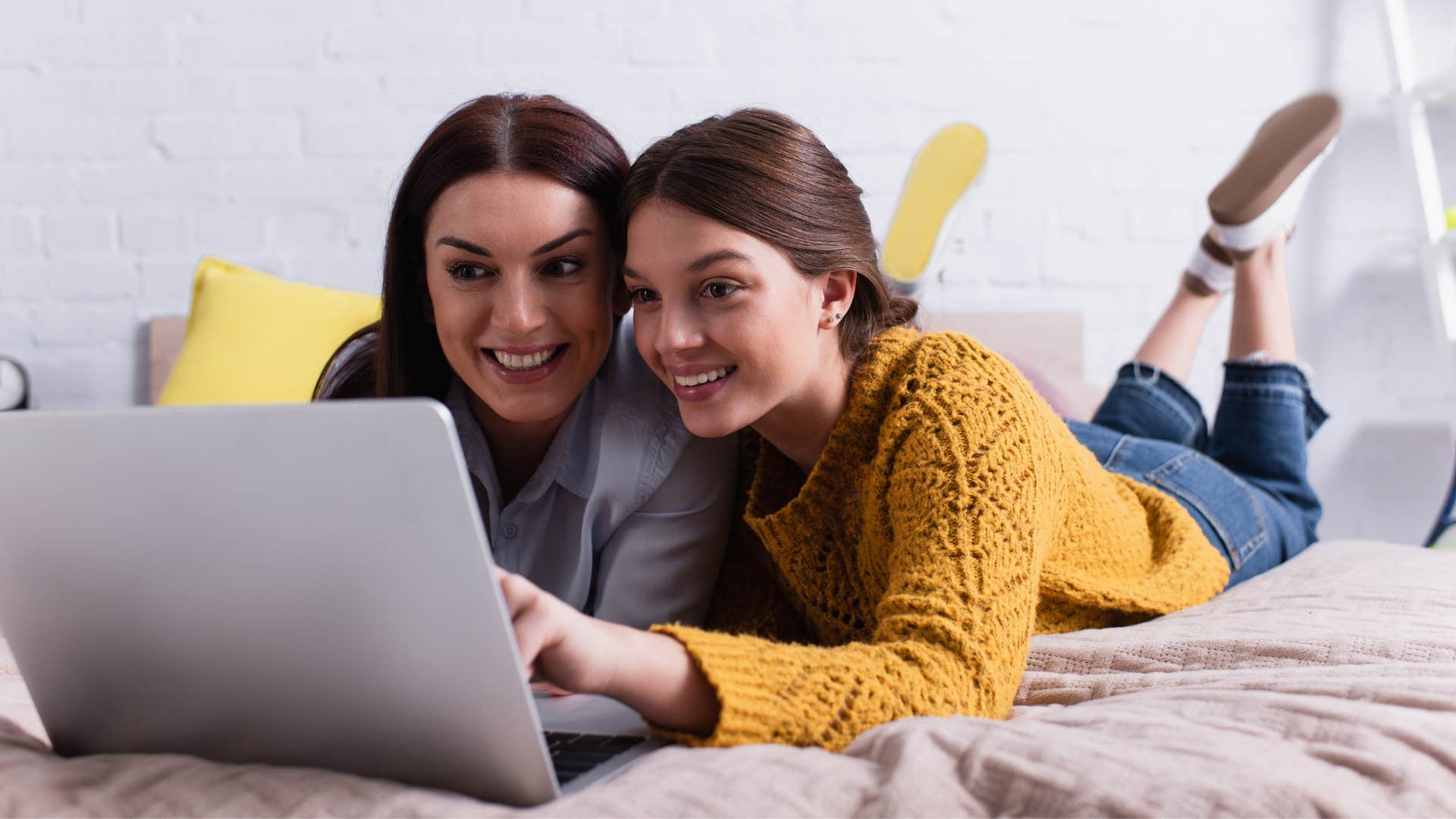 sisters laying on bed watching a movie on a laptop