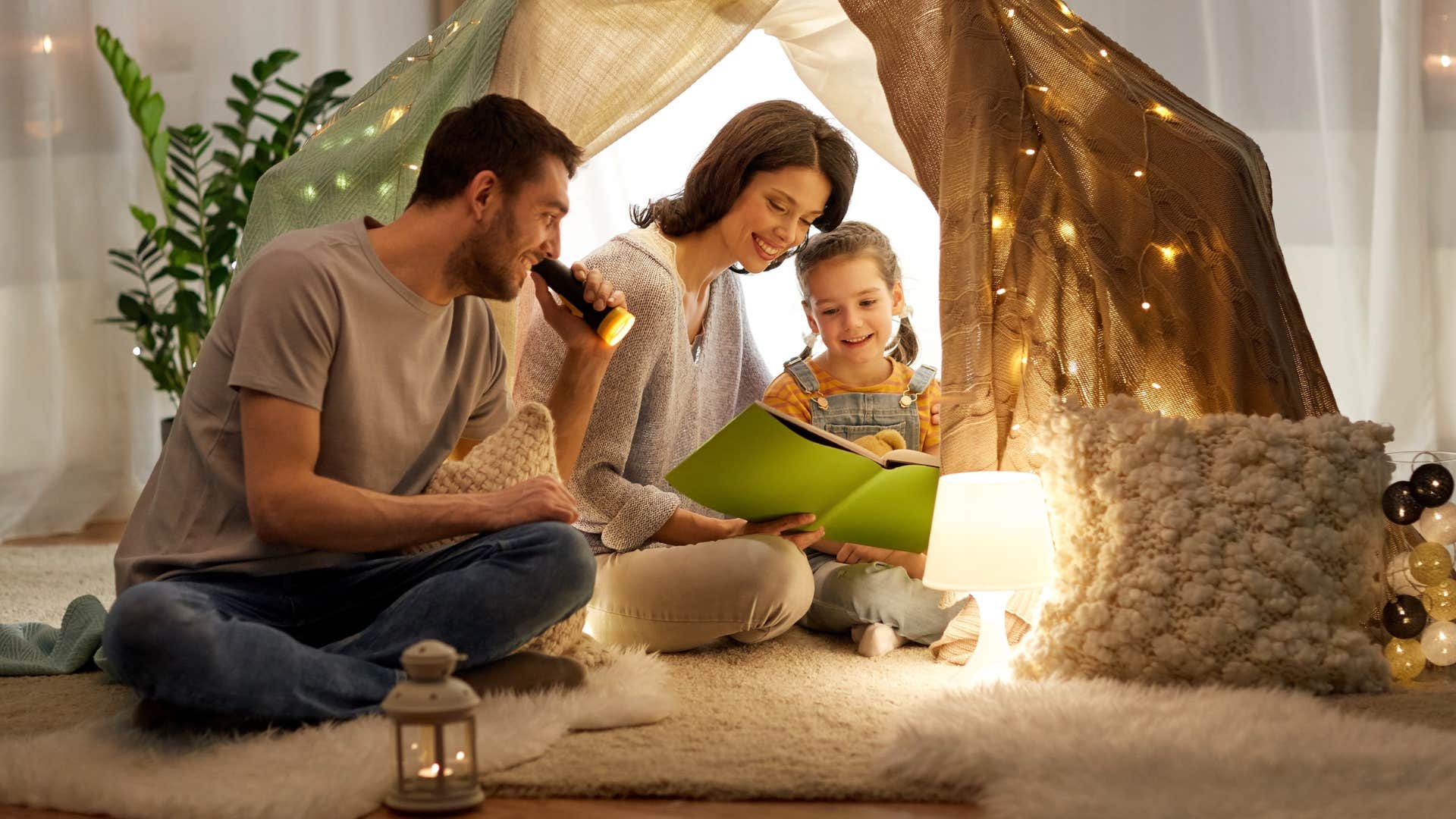 parents telling daughter a story in a lit up tent