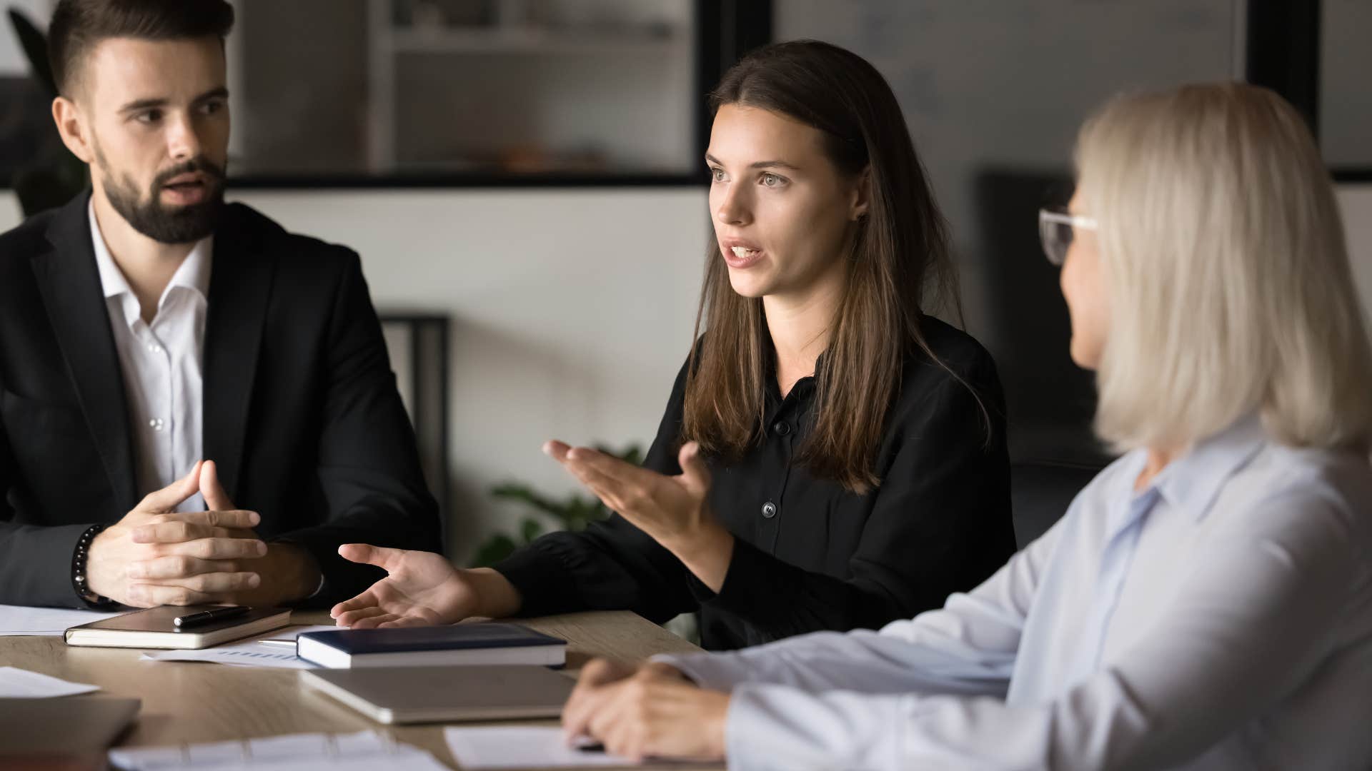 woman in black telling coworkers in a meeting i hear what you'e saying, but let's wrap this up soon to avoid wasting too much time
