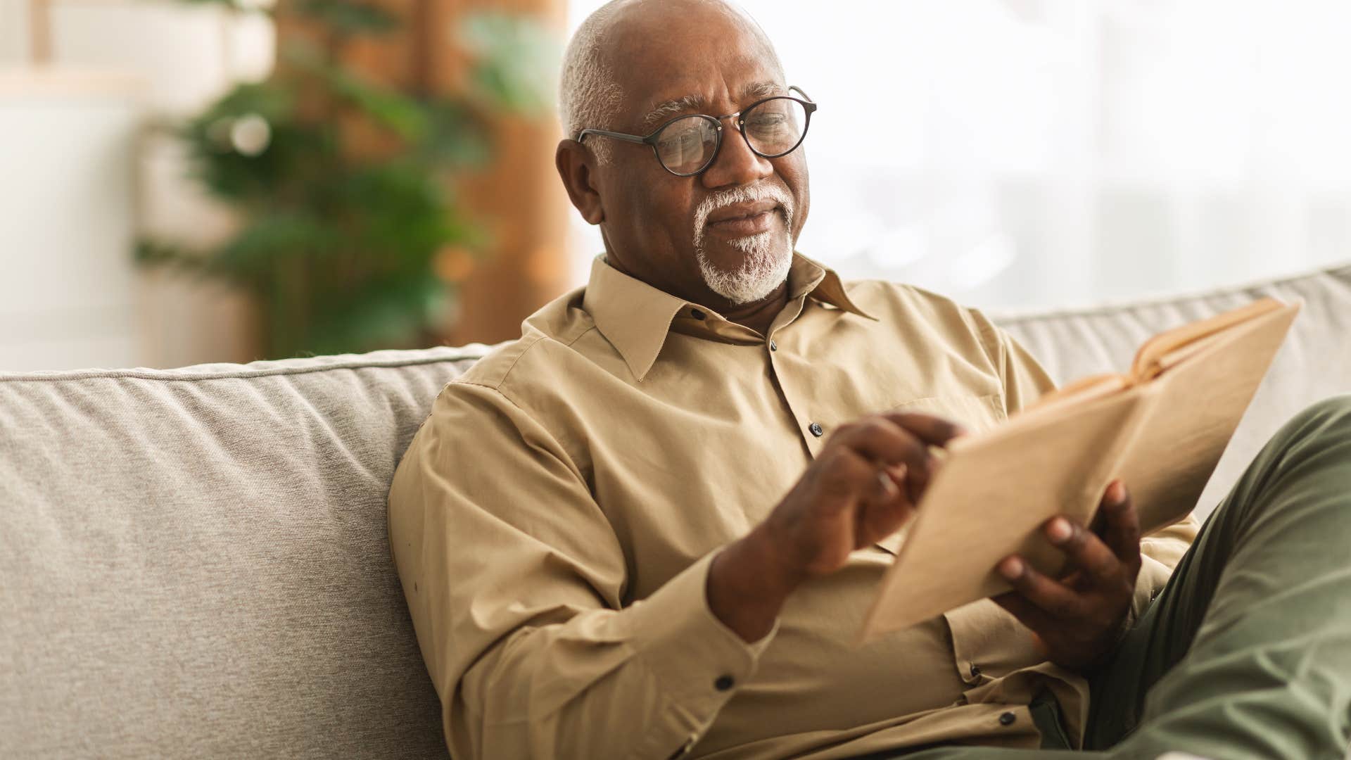 older man sitting on couch reading book