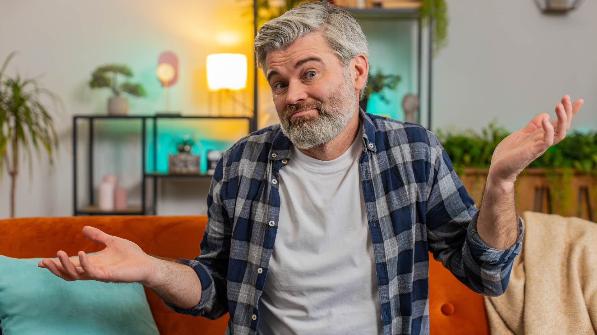 man shrugging and saying i don't know as he sits on the couch in his gray shirt 