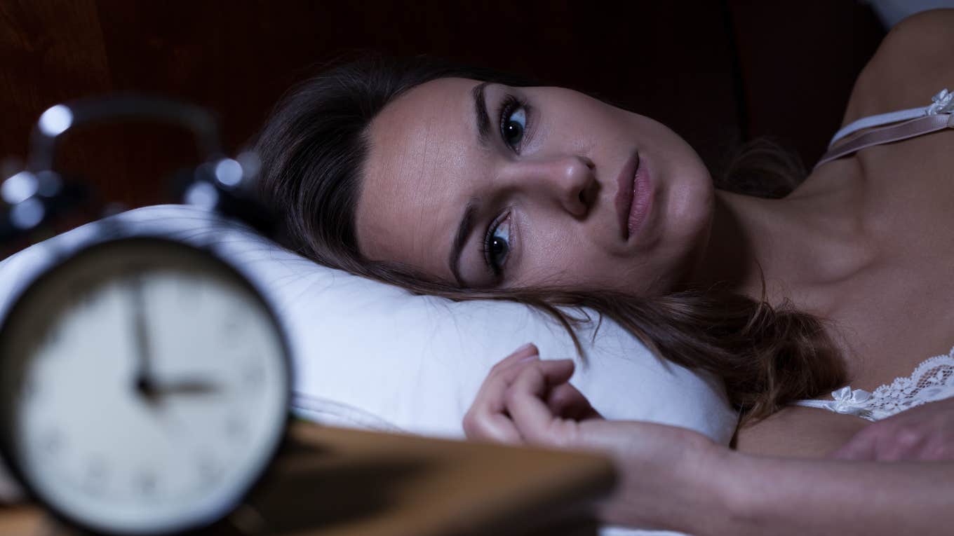 brilliant woman struggling to fall asleep looking at the clock
