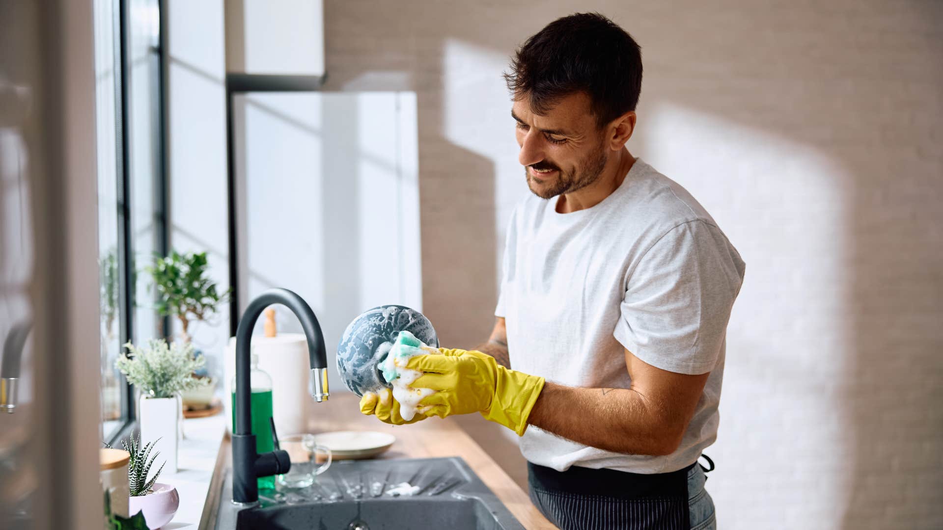 man in white shirt doing his fair share of household responsibilities without being asked to as he washes dishes