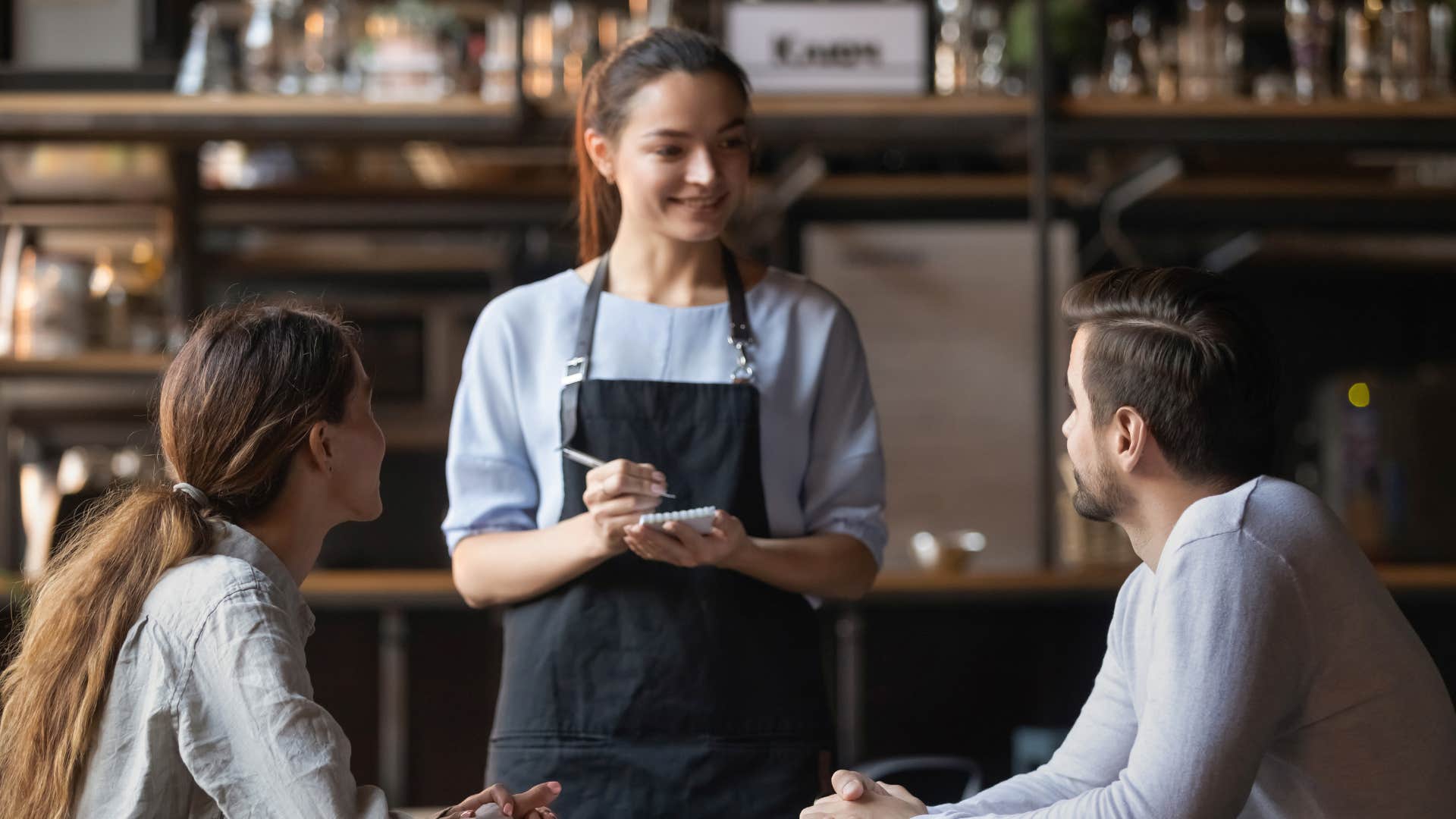 man treating waitress with respect as waitress takes couple in gray shirt order