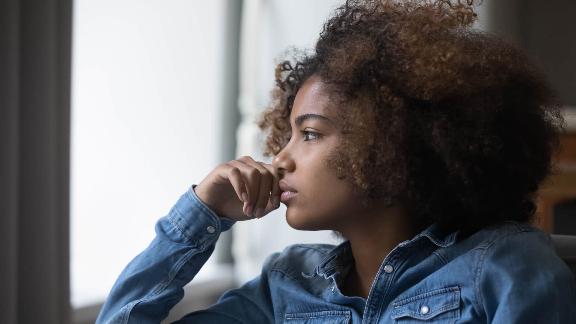 woman in jean shirt stops sharing her inner world as she looks out the window in deep thought