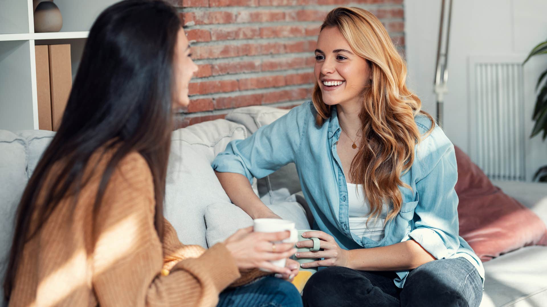 woman in denim jacket saying bless your heart to friend in brown sweater as she smiles