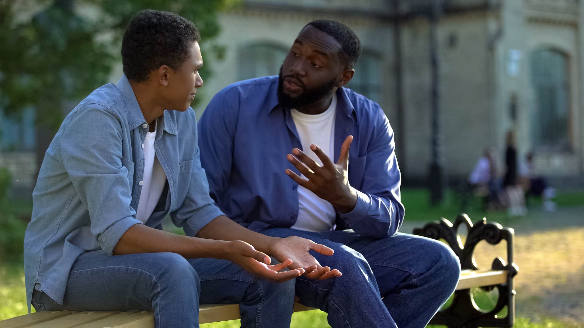 father in dark blue jacket warning son to just keep on as sun in light blue shirt argues back