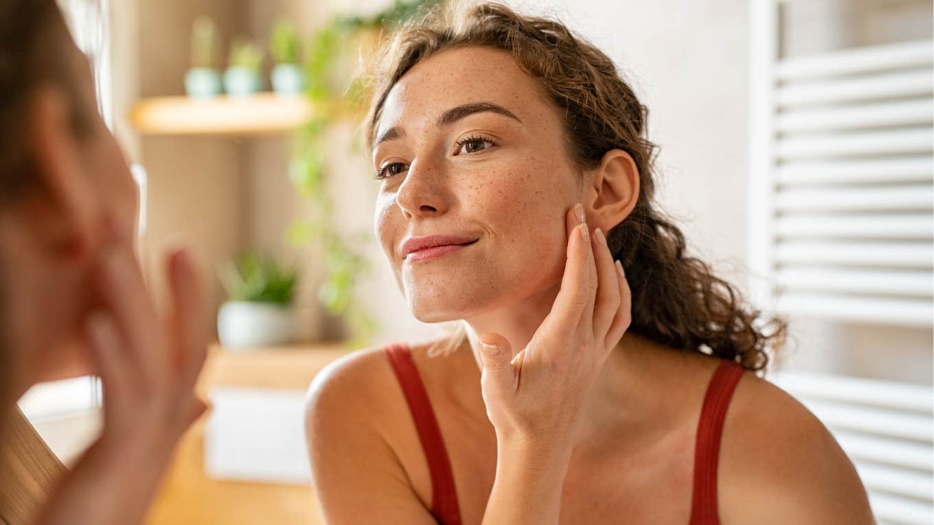 Things That Are Extremely Unsanitary, But Most People Still Do Them Anyway woman with unsanitary habits touching face in mirror