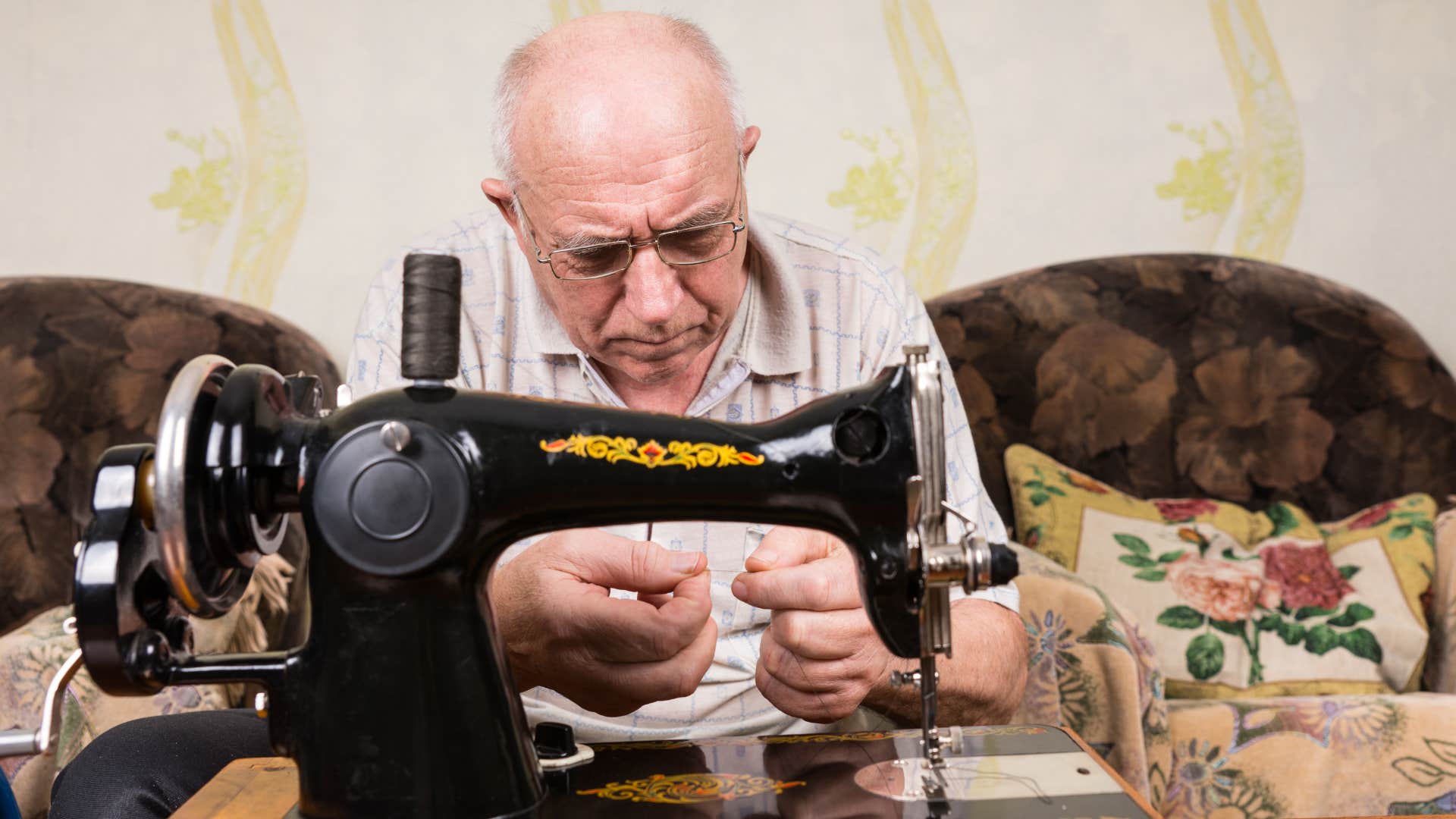 a boomer man tries to resew his pants after ripping them