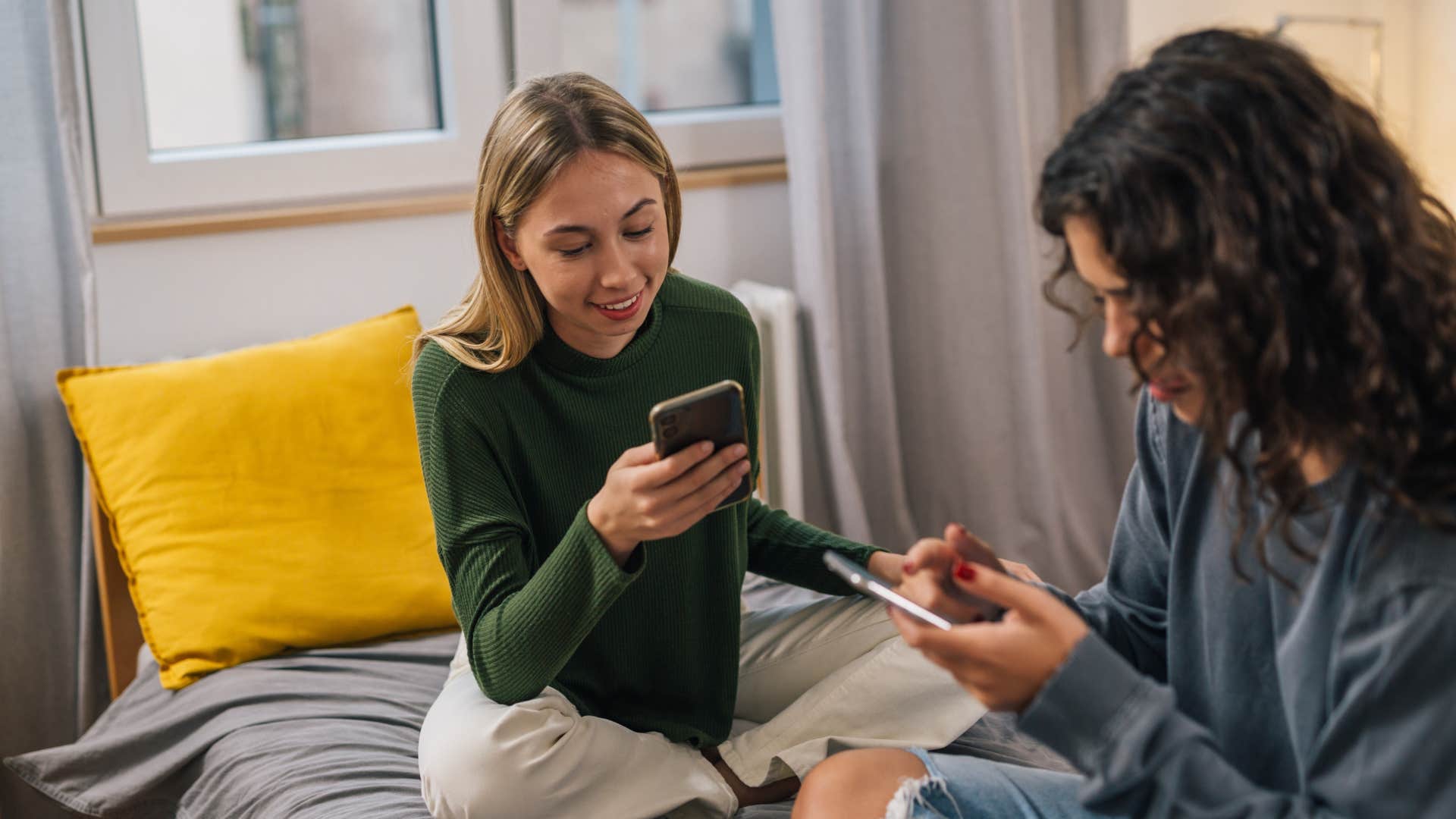 women sitting on bed using their phones