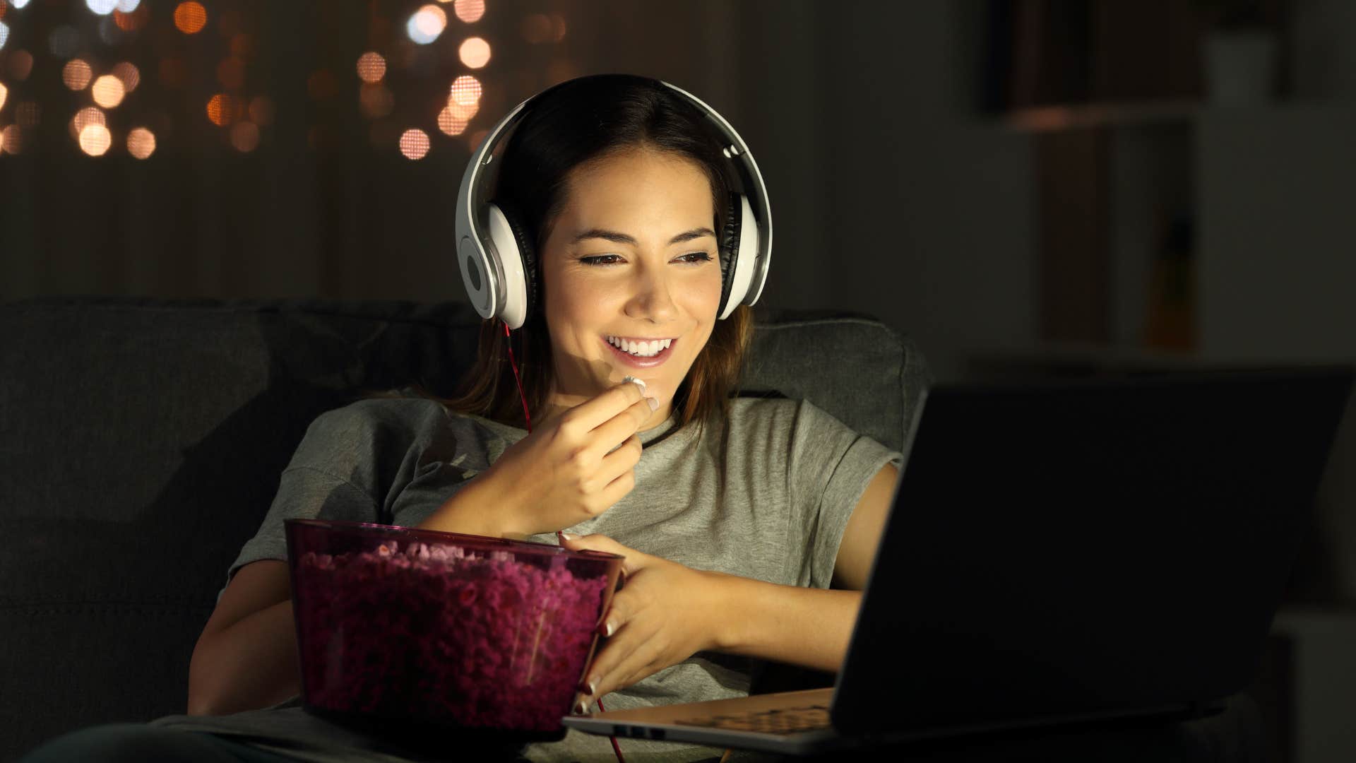 young woman watching tv with headphones on laptop