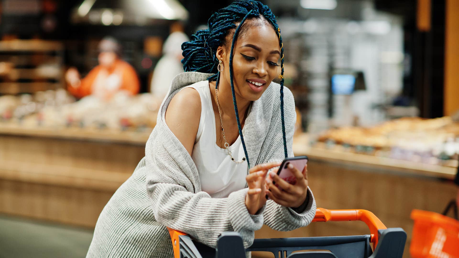 woman looking at her phone while grocery shopping not sticking to a budget