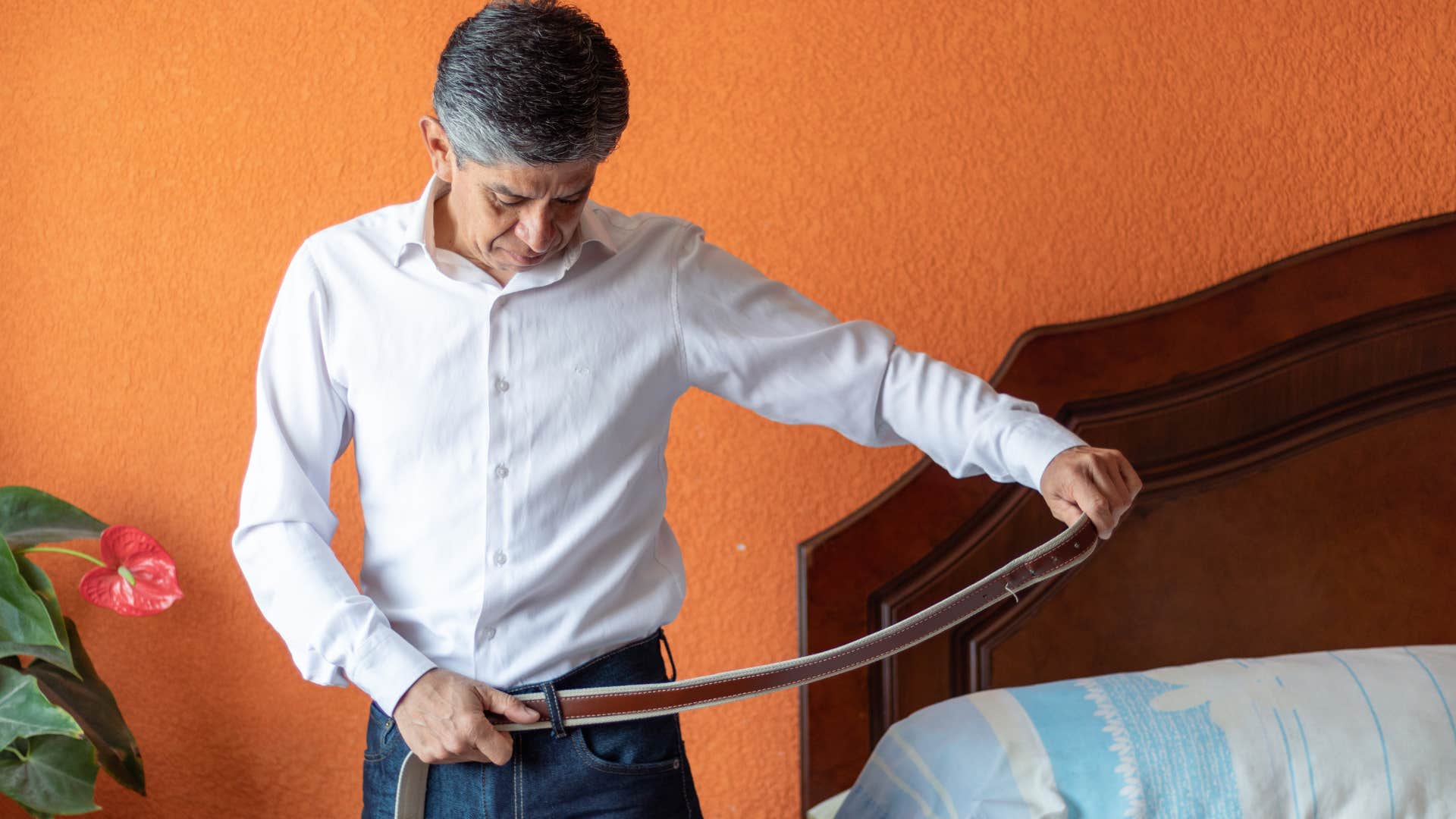 Man putting on a leather belt at home.