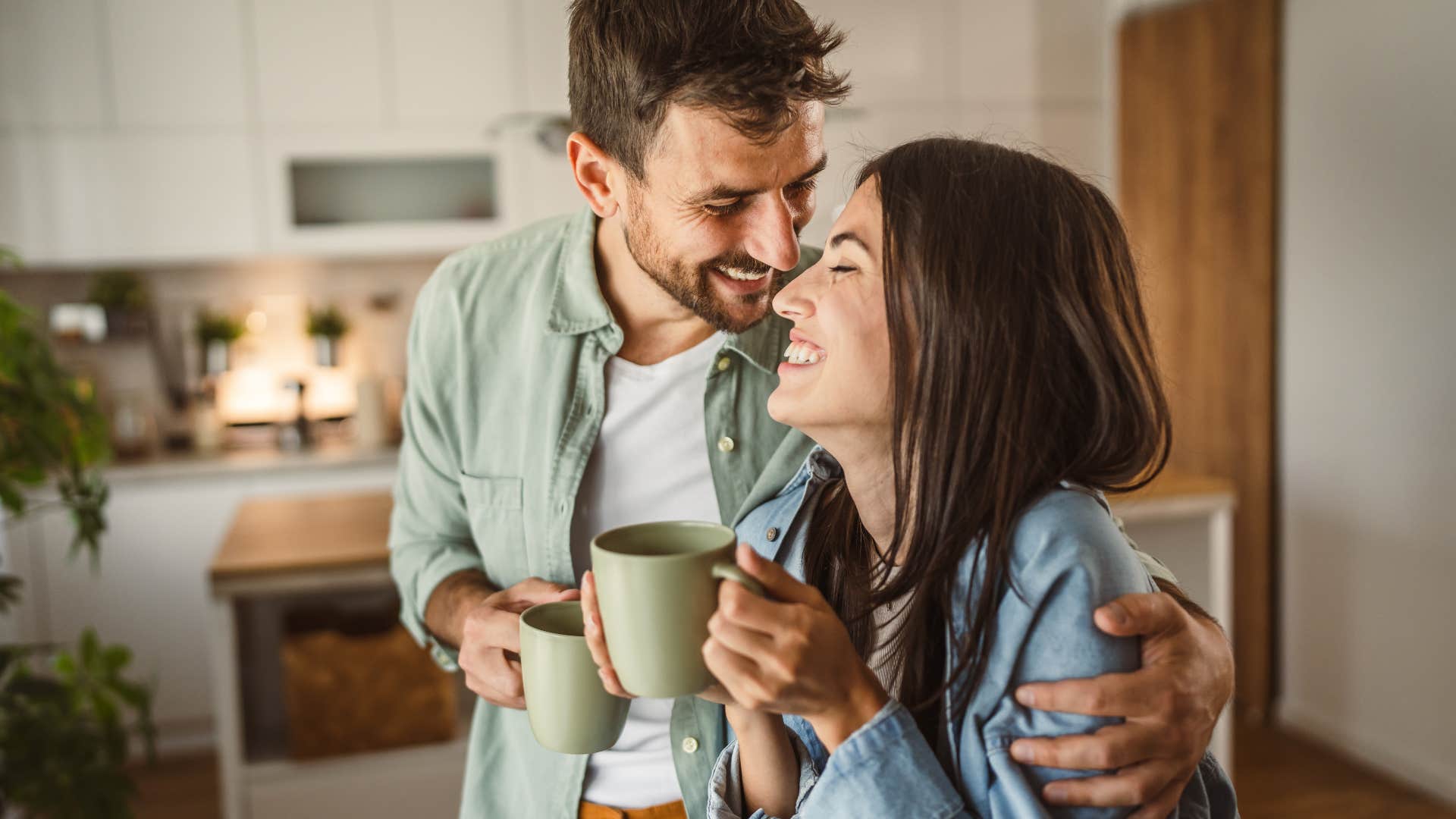 Couple smiling and drinking out of coffee mugs together.