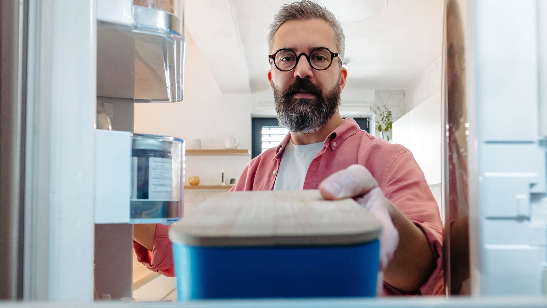 Man putting food containers into his fridge.