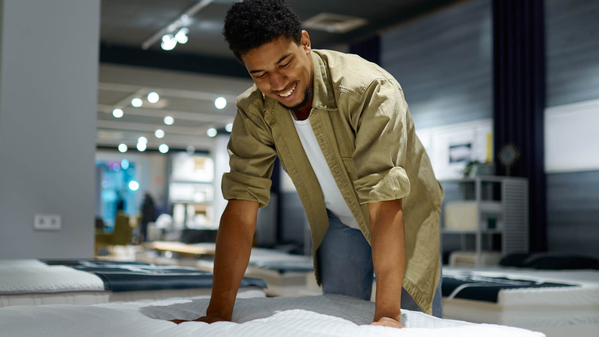 Man smiling and feeling a mattress in a store.