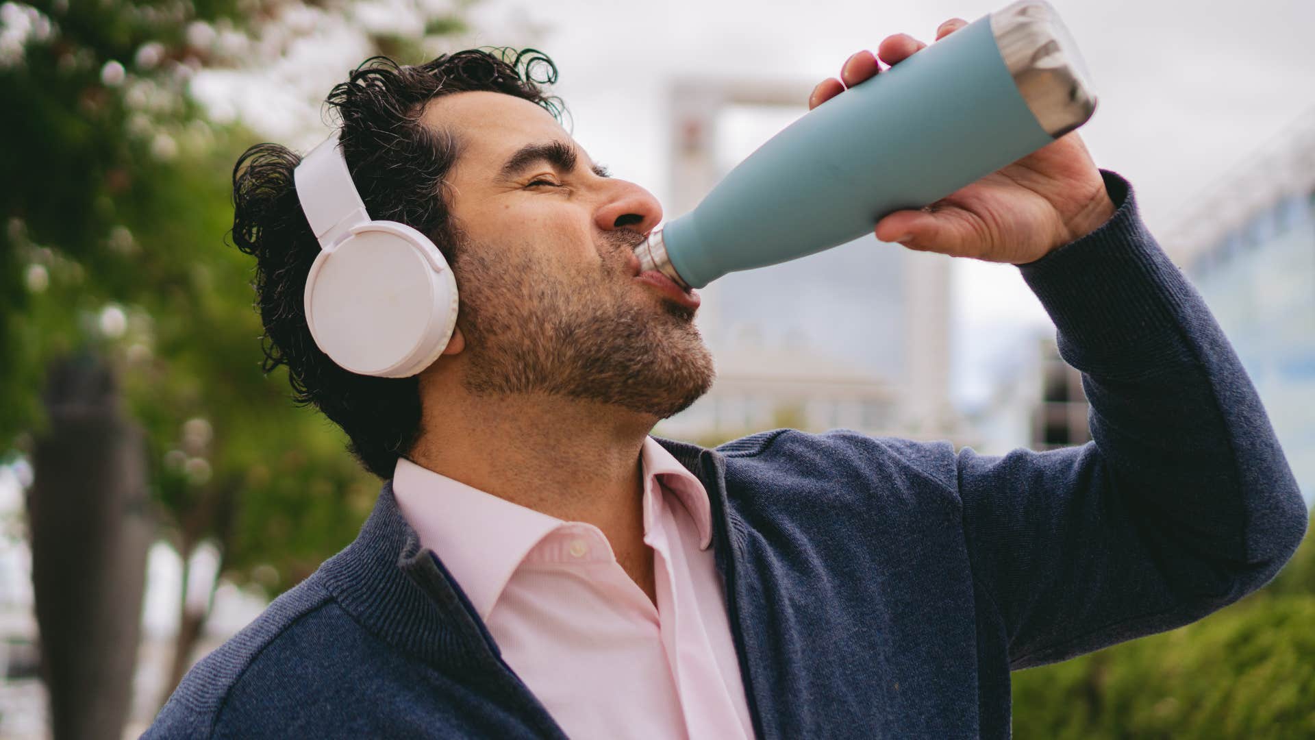 Man drinking from a reusable water bottle outside.