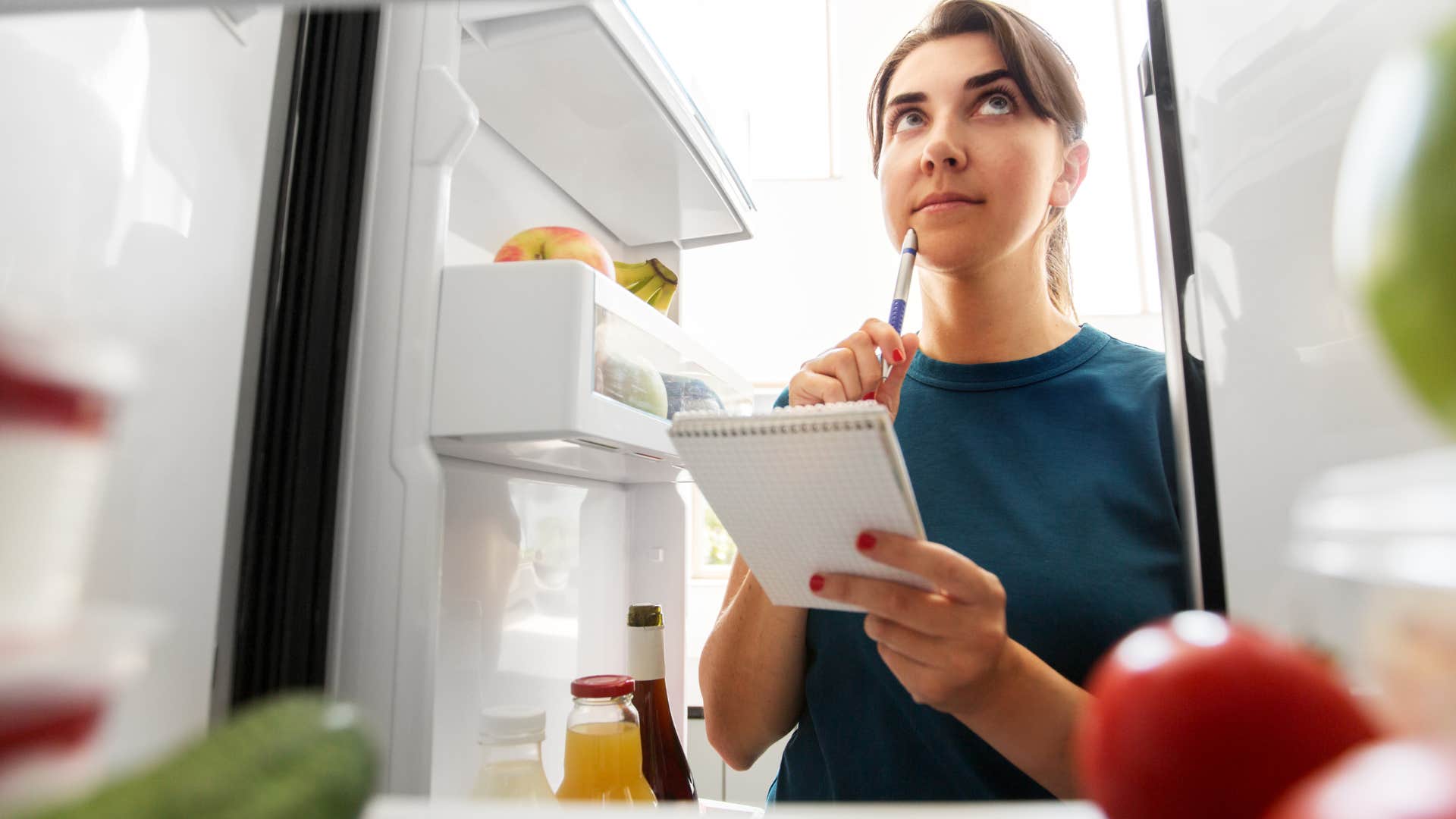 woman making a fridge inventory list looking at her groceries