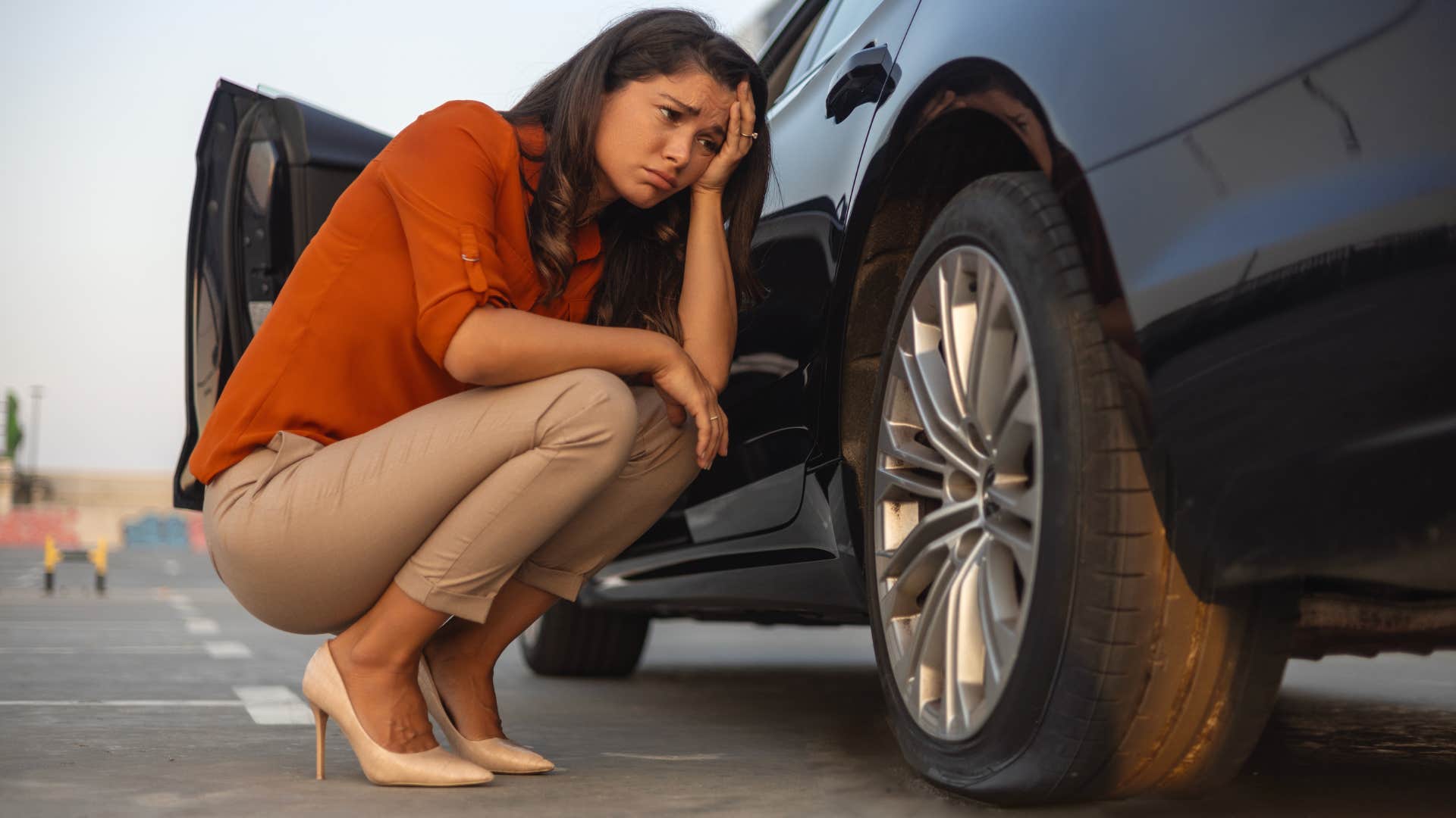 frugal woman in heels looking sad at flat tire