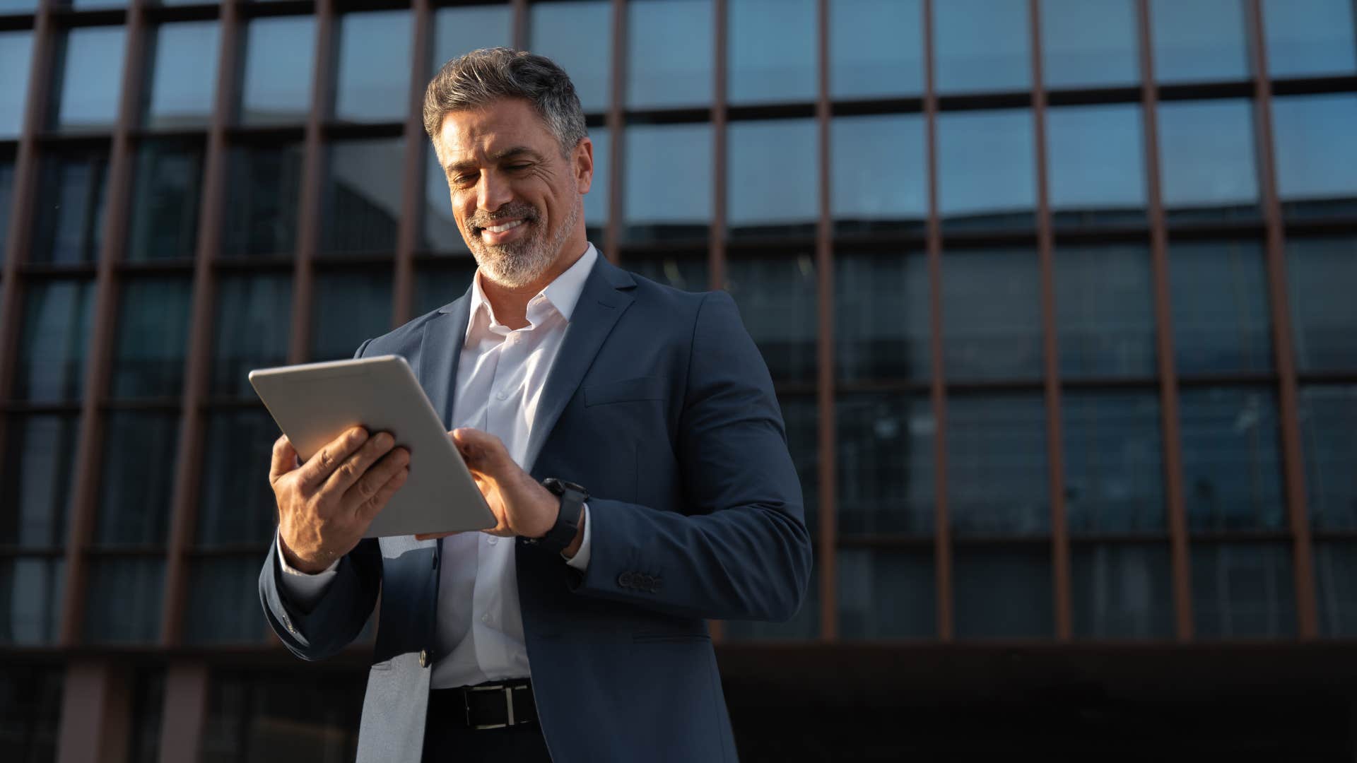 man on ipad always upgrading his technology and he stands in front of building in suit