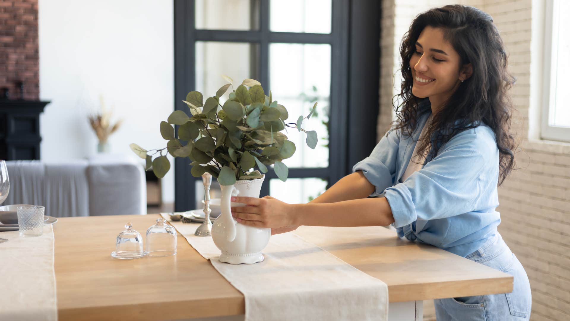 woman in blue shirt always redecorating her spaces as she places plant on table