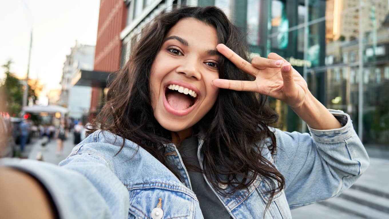 Things Gen Z Sees As Basic Respect That Boomers Still Think Are Overreactions smiling gen z woman making a peace sign for respect