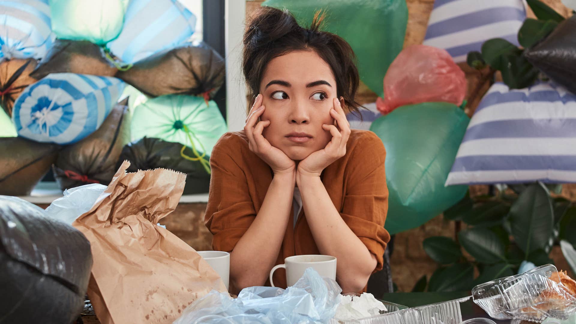Woman sitting at home surrounded by clutter.