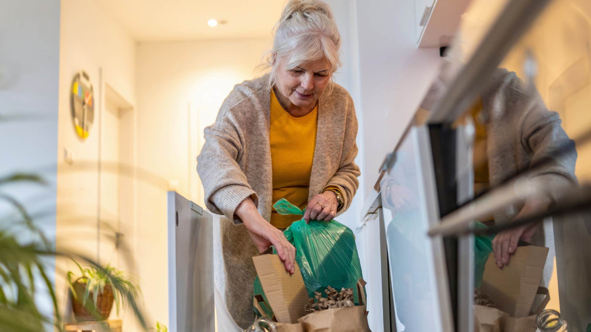Woman putting boxes into an overflowing trash can at home.
