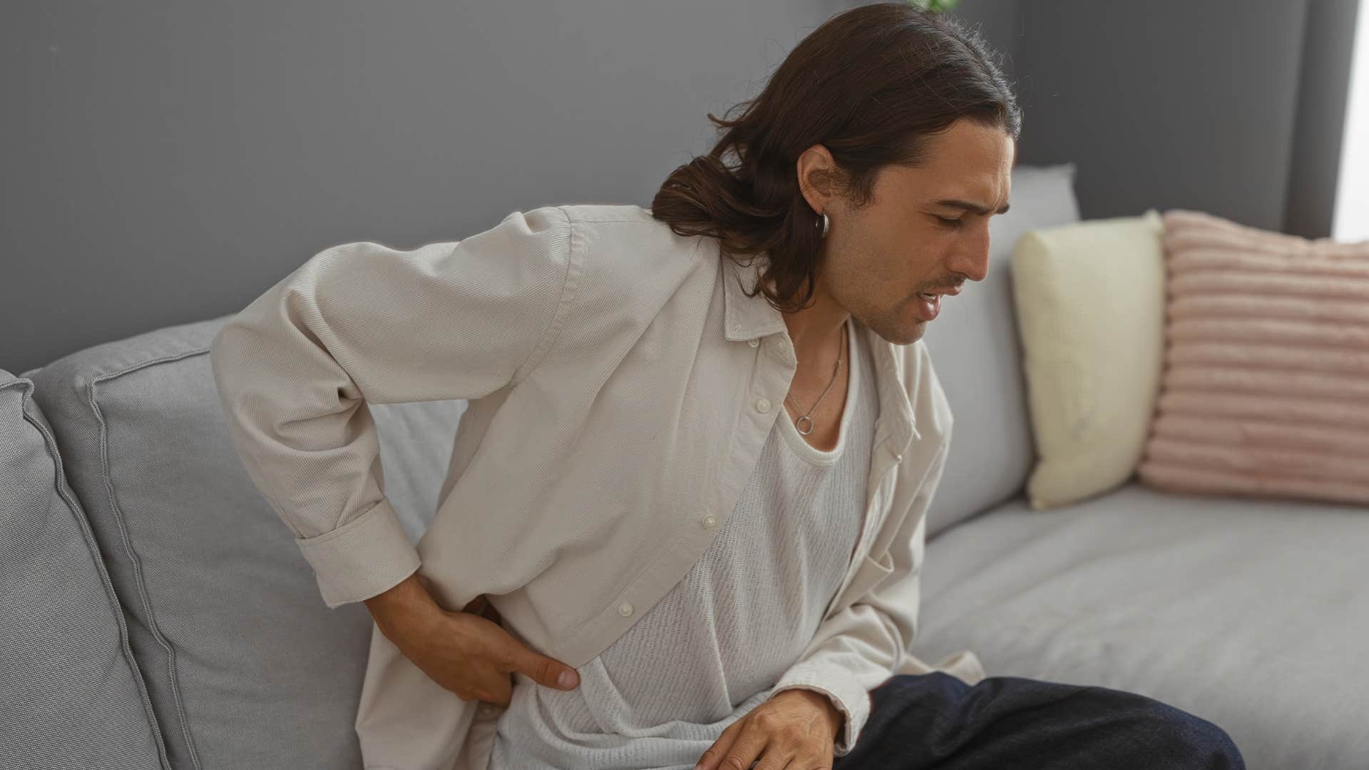 Man sitting on uncomfortable furniture and holding his back.