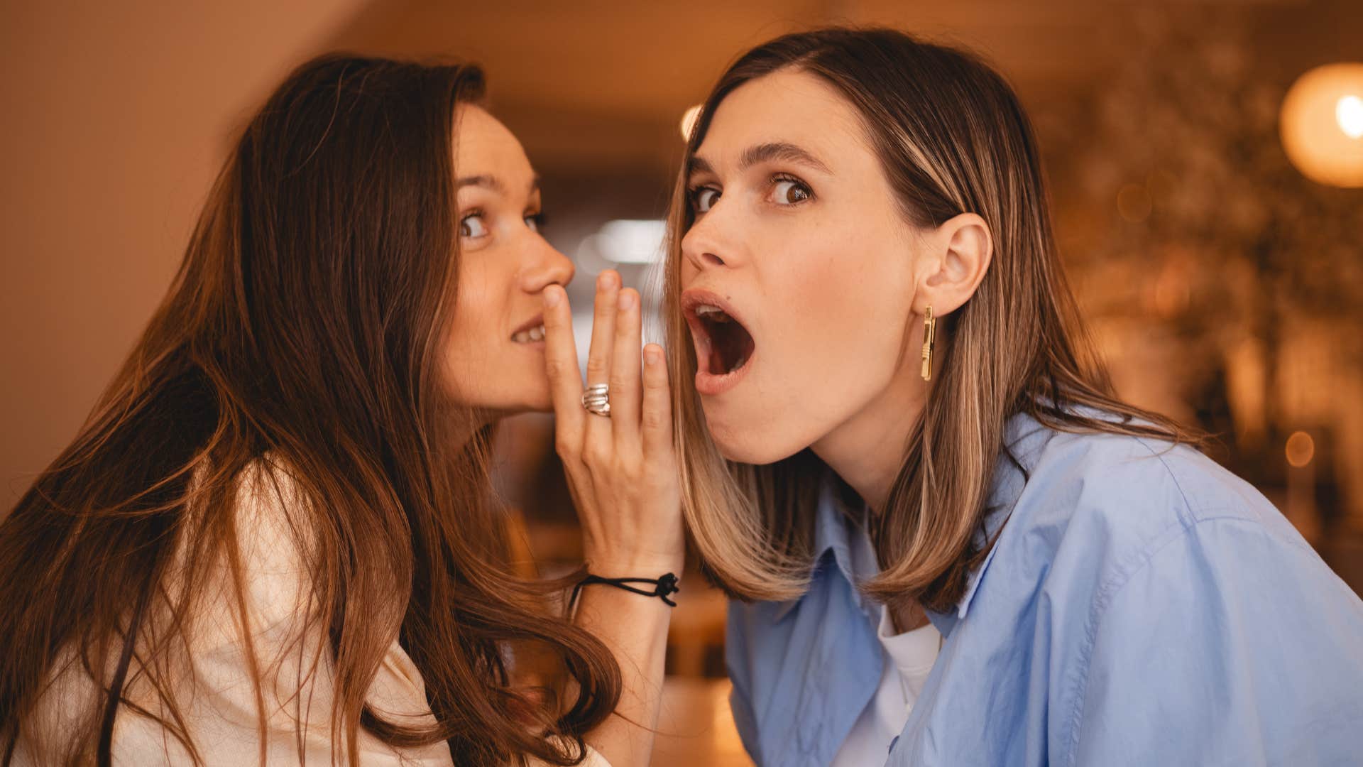 two women gossiping while one woman whispers in blue shirt friends ear and says she's got a big personality