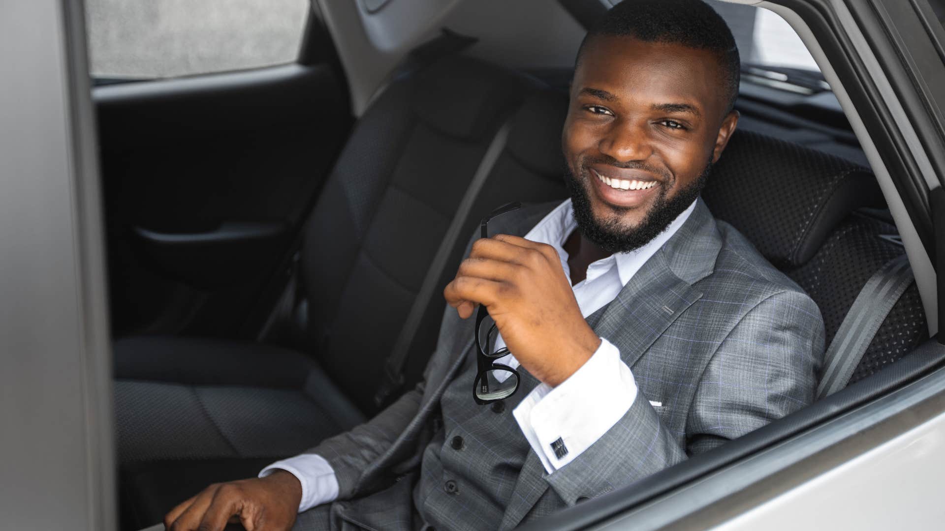 Man flaunting their wealth in the back of a nice car.