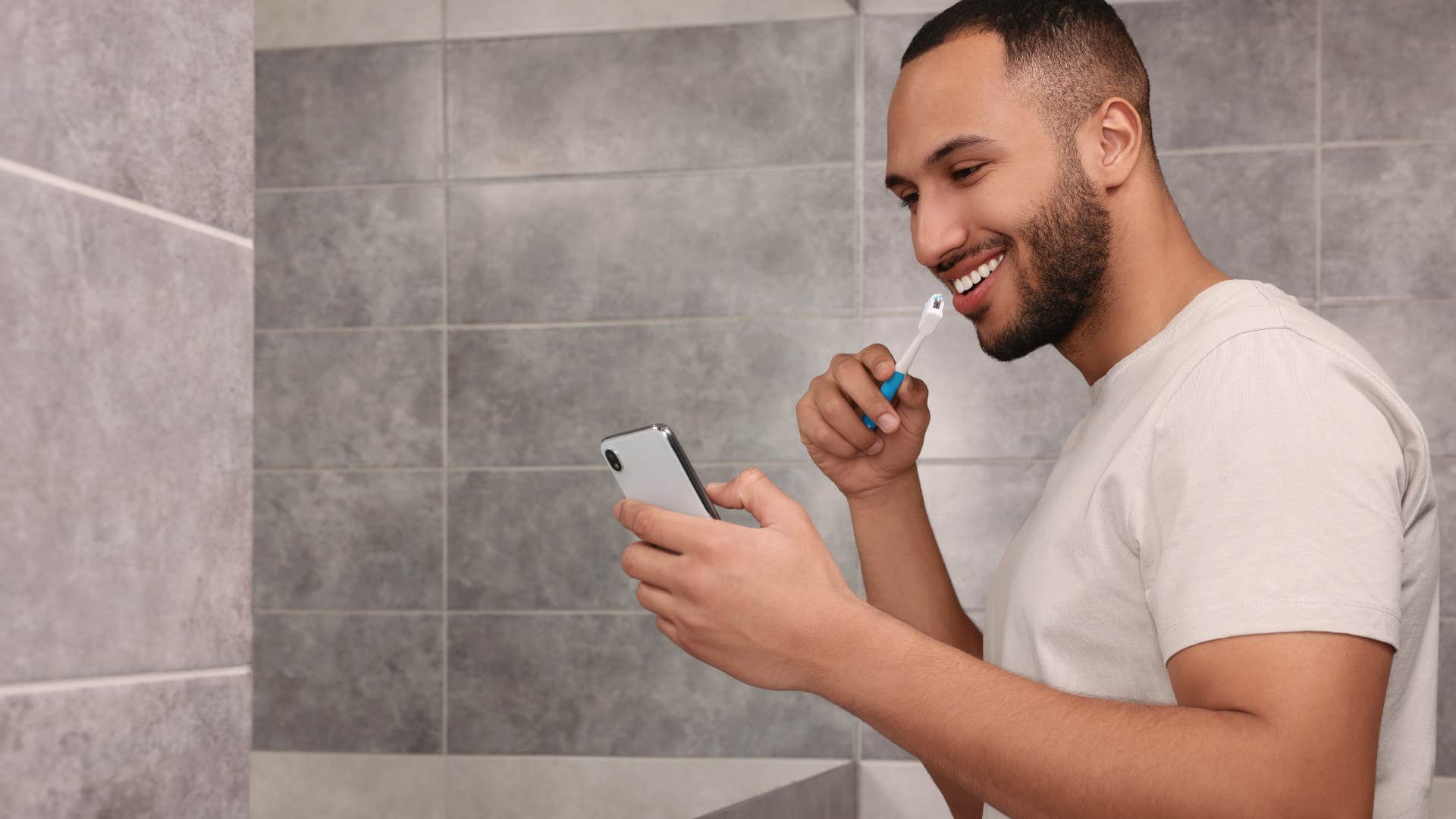 man using his phone in the bathroom brushing his teeth