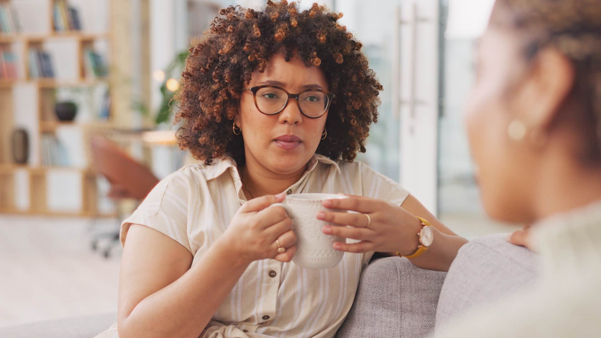 Woman holding a coffee mug and listening to overly critical people talk.