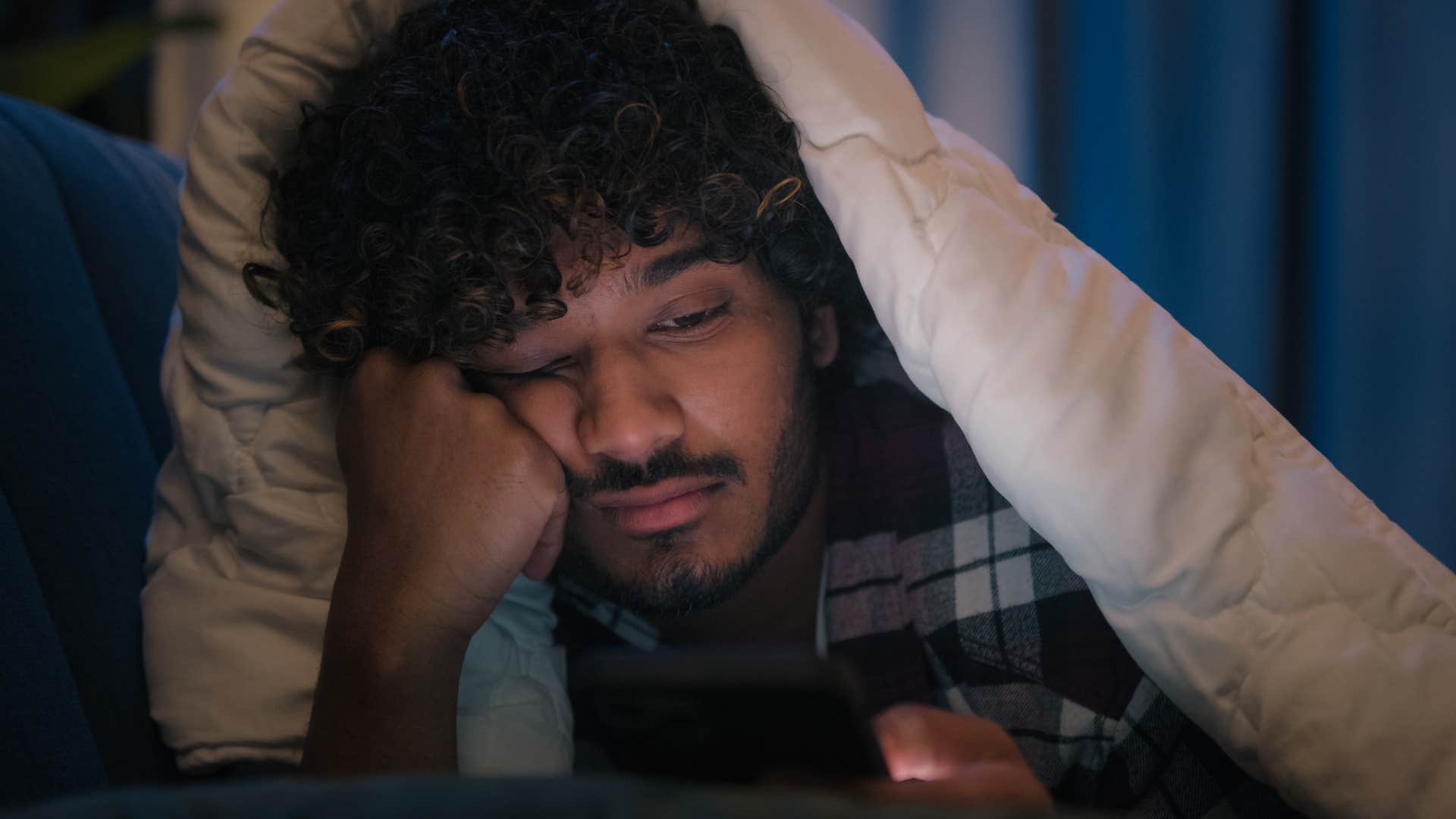 stressed man looking at news headlines in bed