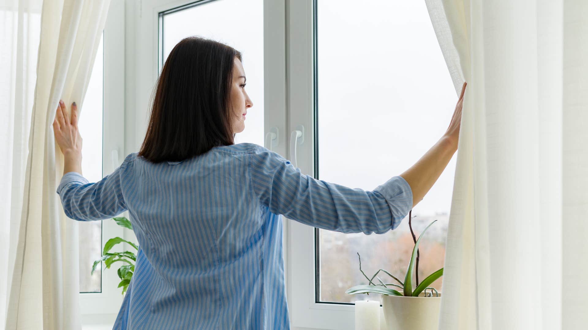 a type a woman opens her friends curtains to allow more natural light into her home