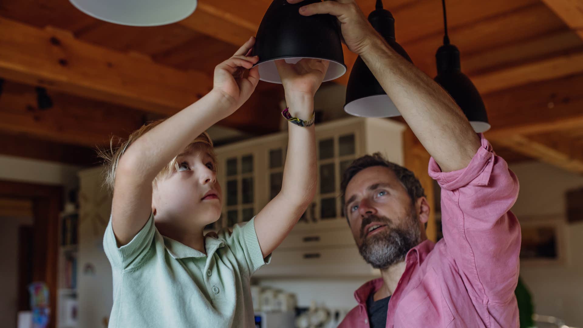 a son helps his father change a lightbulb after his friend notices