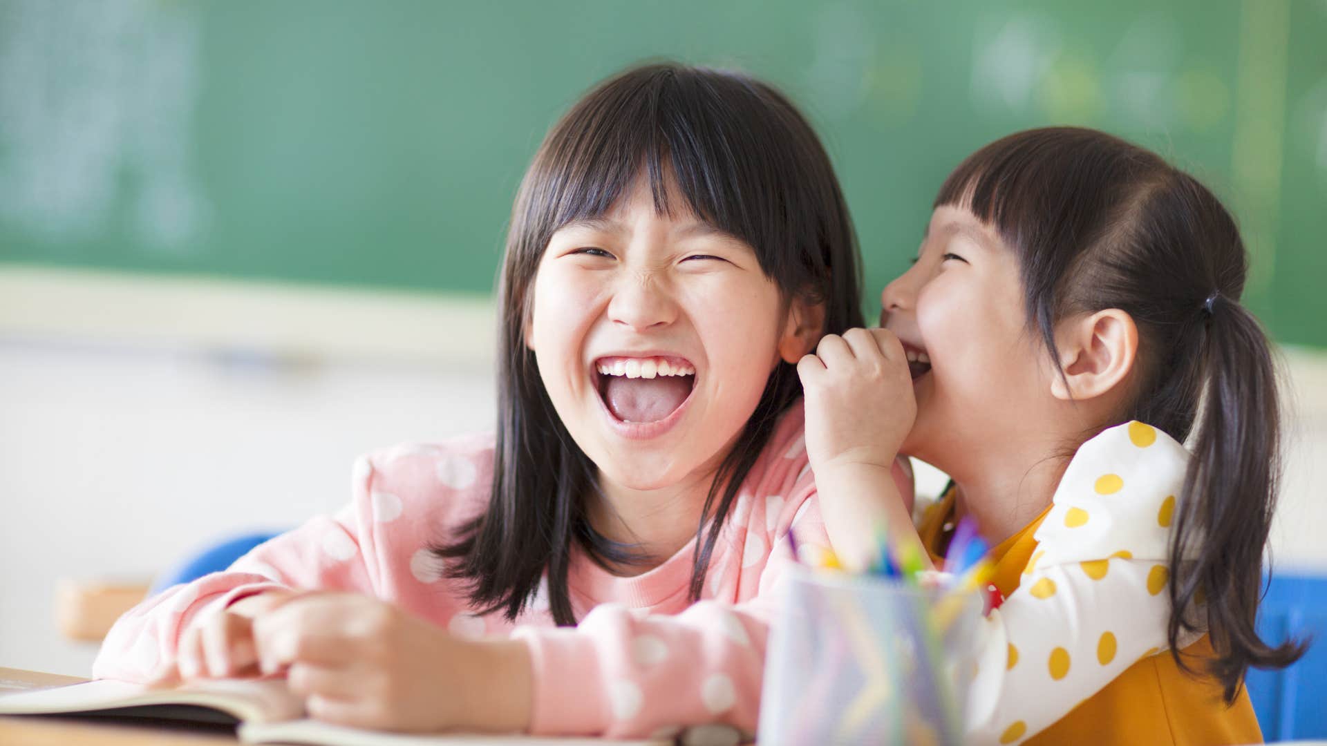 Little girls who gossip about others talking in the classroom.