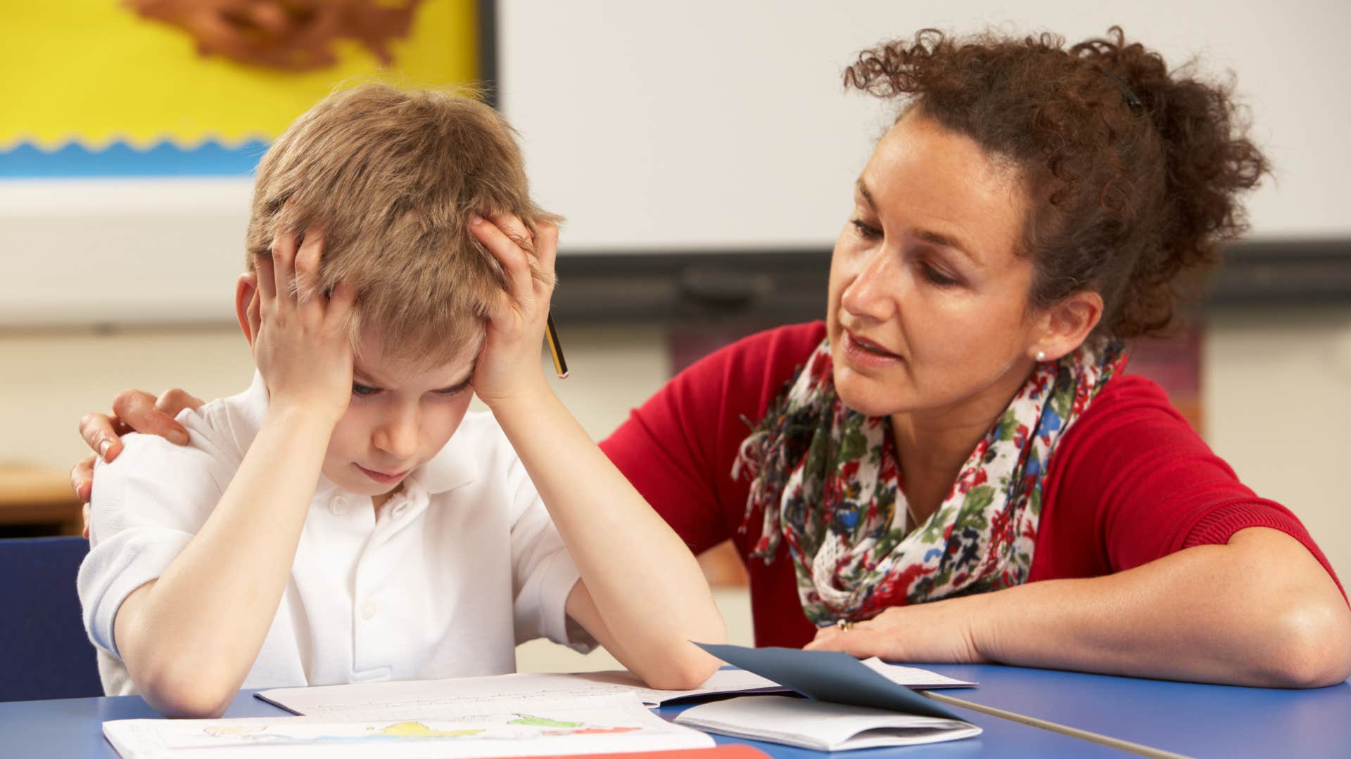 Woman talking to an upset boy who doesn't respect classroom materials.