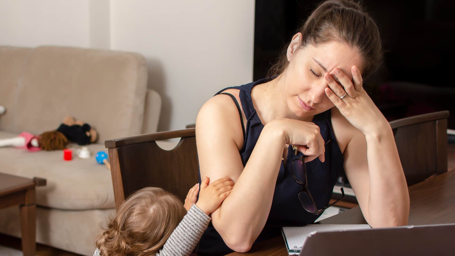 sleep deprived mother holding her head next to her toddler