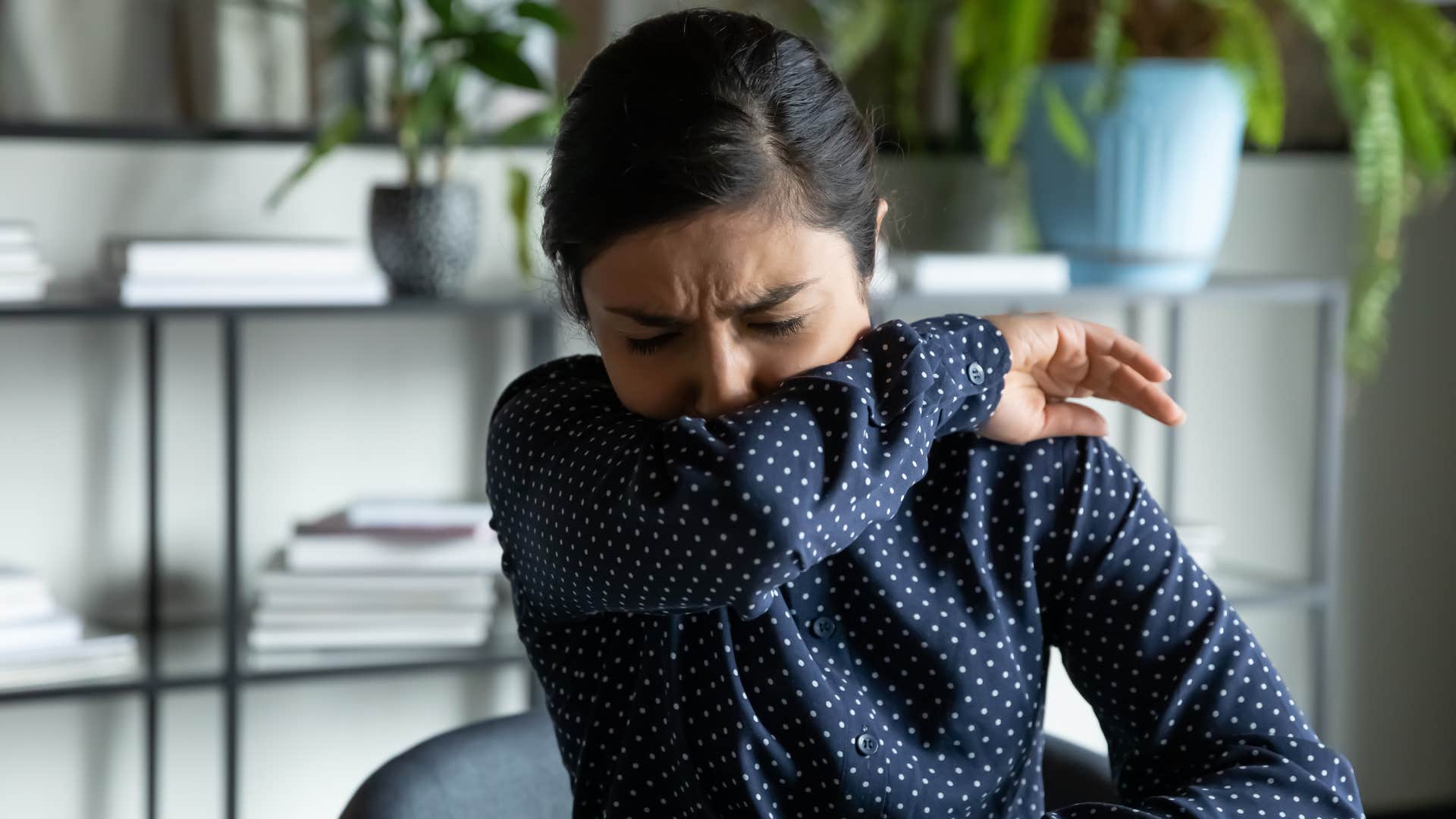 a young woman covers her nose and mouth as she sneezes to prevent germs from spreading